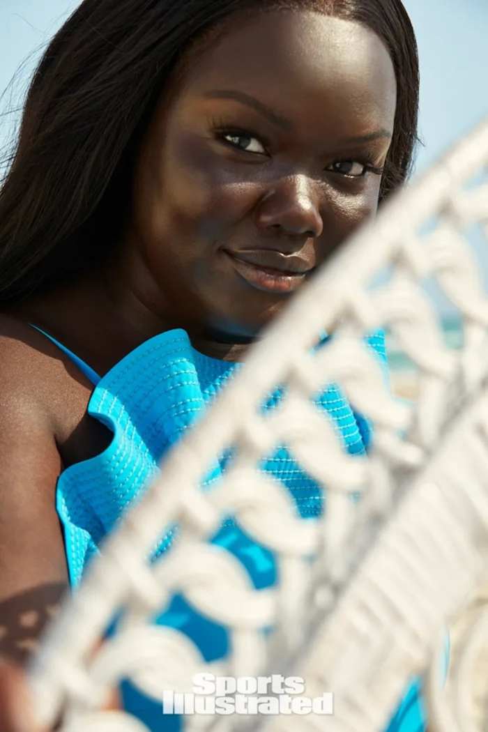 Nyma Tang poses in a vibrant blue bikini behind a white chair.